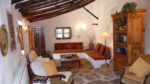 A cozy living room with a stone floor, a wooden ceiling, a sofa, a coffee table, and a bookshelf.