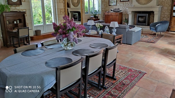 Un salon spacieux doté d’une cheminée, de murs en pierre et d’un coin repas avec une table mise pour quatre personnes.