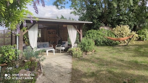 Un espace extérieur aménagé avec des meubles de jardin, comprenant une table et des chaises, le tout à l’abri, et entouré d’une végétation luxuriante et d’un hamac.