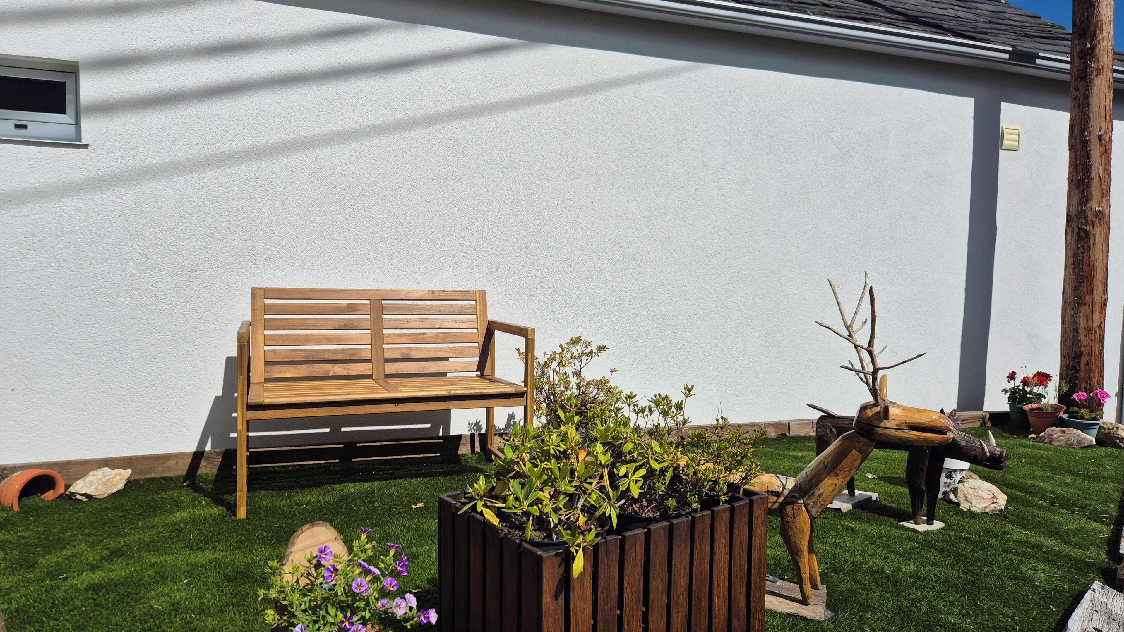 Un banco de madera, una maceta con flores y una escultura de madera en un jardín.