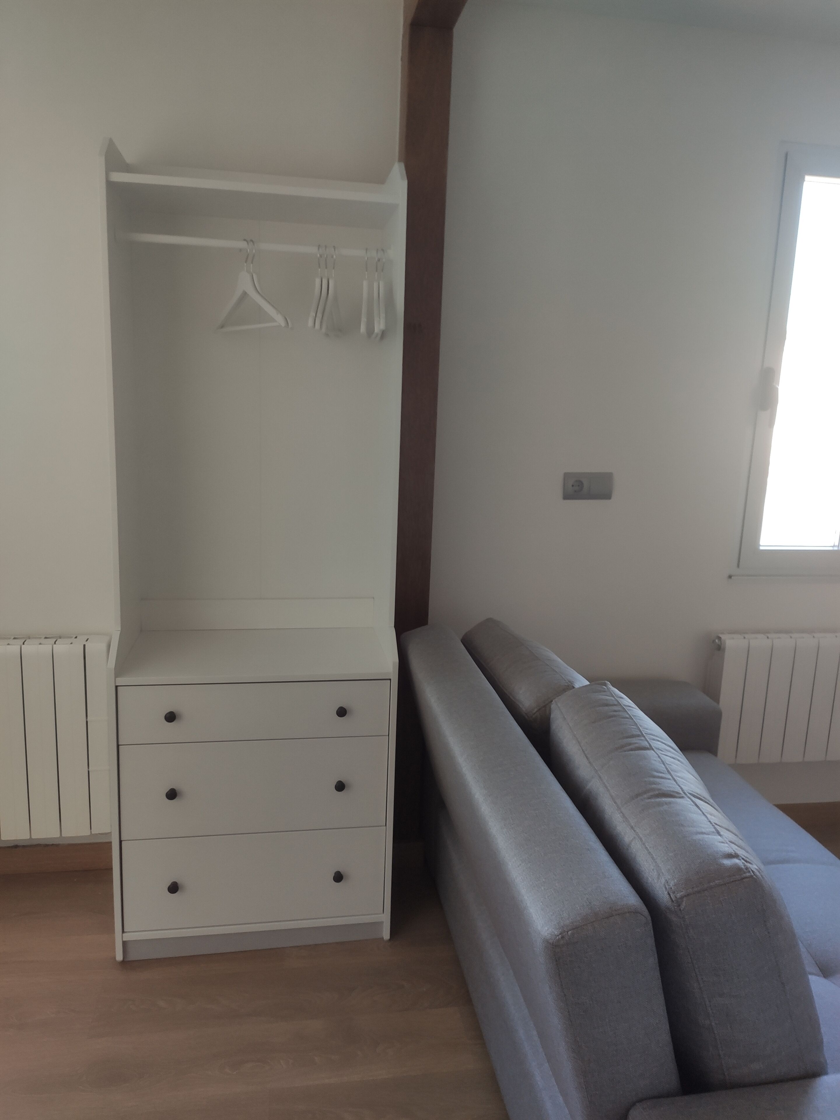 Une pièce avec une armoire blanche, un canapé gris et une fenêtre.