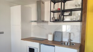 Cocina compacta con muebles blancos, microondas integrado, lavavajillas, pileta de acero inoxidable y repisa negra sobre la encimera.