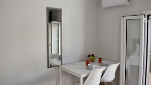 Una petita zona de dinar amb una taula i dues cadires, un bol de fruita i un aparell d'aire acondicionat blanc a la part superior.