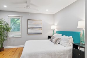 A bedroom with a bed, bedside lamps, a ceiling fan, a window with blinds, and a framed picture on the wall.