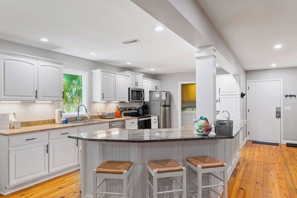 A modern kitchen with white cabinetry, a central island with stools, stainless steel appliances, and a wooden floor.