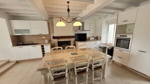 Een moderne keuken met witte kastjes, een eettafel met stoelen, een kroonluchter en een inbouwoven.