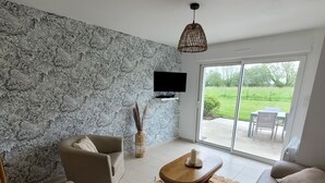 Een moderne woonkamer met een wand met een stenen patroon, een flatscreen televisie, een bank, een bijzettafeltje en uitzicht door grote schuifdeuren op een buitenruimte.