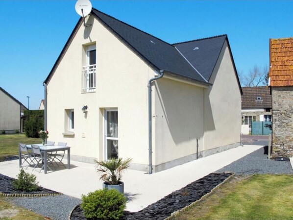 A two-story house with a sloped roof, a satellite dish, and a small patio with a table and chairs.