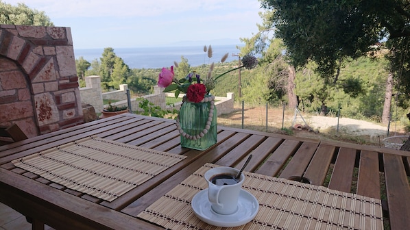 A wooden table with a woven placemat, a white cup with a spoon, and a green vase with flowers.