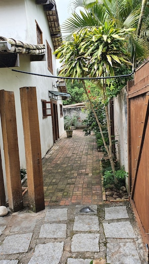 Um caminho de tijolos estreito que leva a um edifício branco com pilares de madeira e um portão de metal.