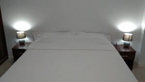 A neatly made bed with a white bedspread, flanked by two bedside tables with lamps. - 2 apartments, of 2 rooms each, next each other, for max 10 persons, beachfront (Navodari)