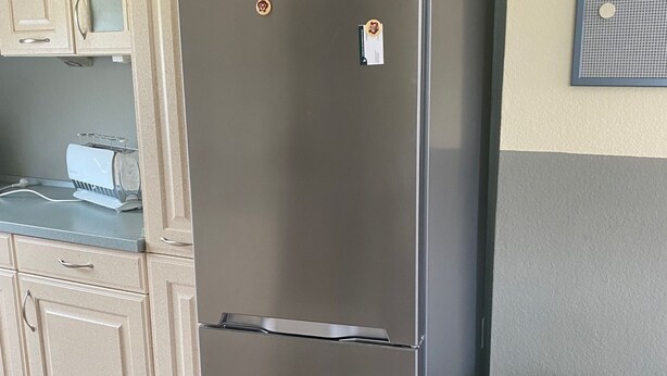 Un réfrigérateur en acier inoxydable dans une cuisine aux armoires beiges et au comptoir gris.