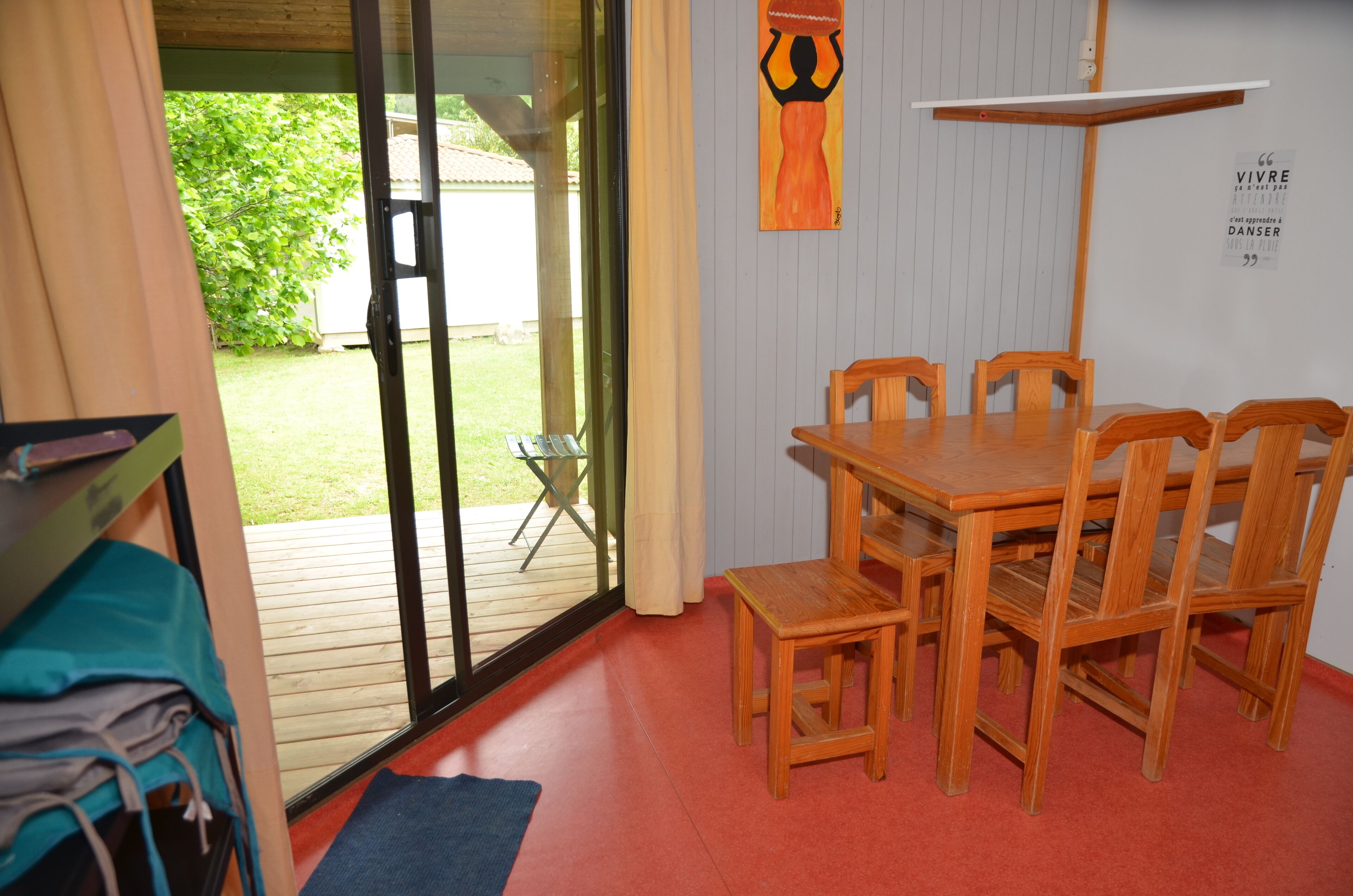 Une pièce avec une table et des chaises en bois, une porte-fenêtre coulissante donnant sur une terrasse, et un tapis bleu sur le sol.