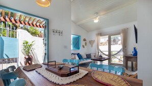 Amplia habitación con una mesa de madera para comer, sillas azules, un sofá y un ventanal con vistas al exterior.