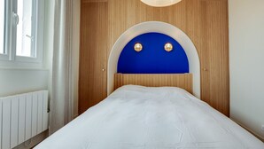 Ein Schlafzimmer mit einem weißen Bett, einem hölzernen Kopfende mit einem blauen Bogen und einer weißen Heizung.