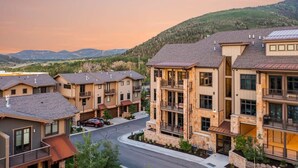Un quartier résidentiel composé de maisons modernes à plusieurs étages, dotées de balcons et de grandes fenêtres, le tout se dressant sur un fond de collines et sous un ciel dégagé.