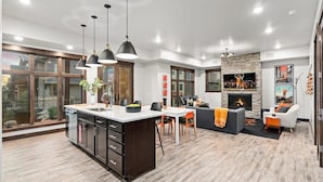 Une cuisine moderne dotée d’un grand îlot central, de luminaires suspendus et d’une cheminée en pierre.