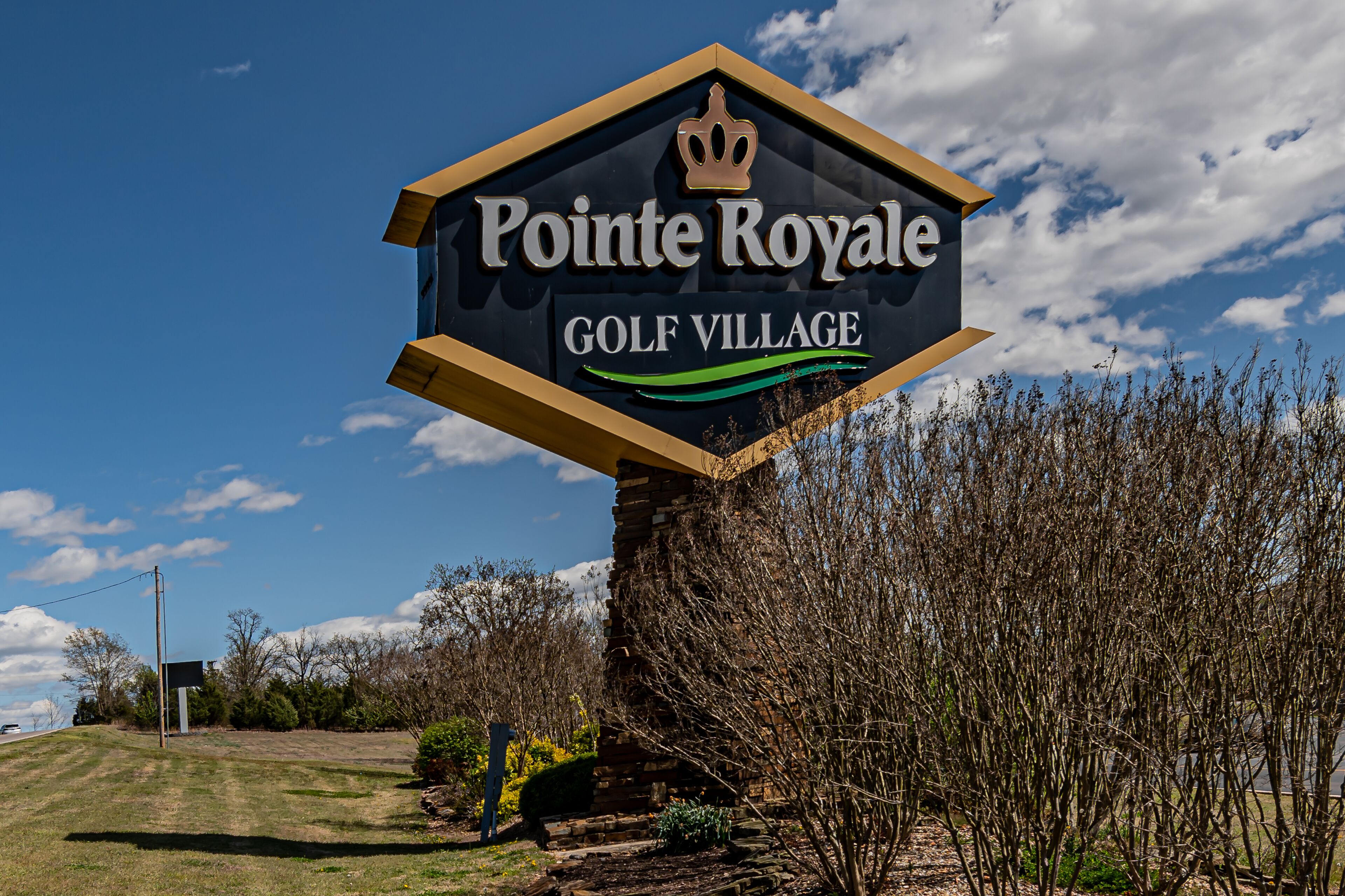 A sign for Pointe Royale Golf Village with a clear sky and trees in the background.