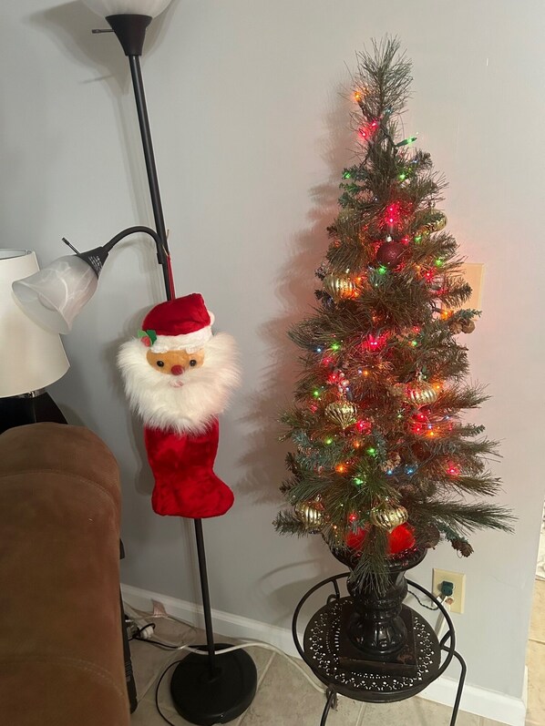 Un árbol de Navidad con luces y adornos, una decoración de Papá Noel y una lámpara de pie.