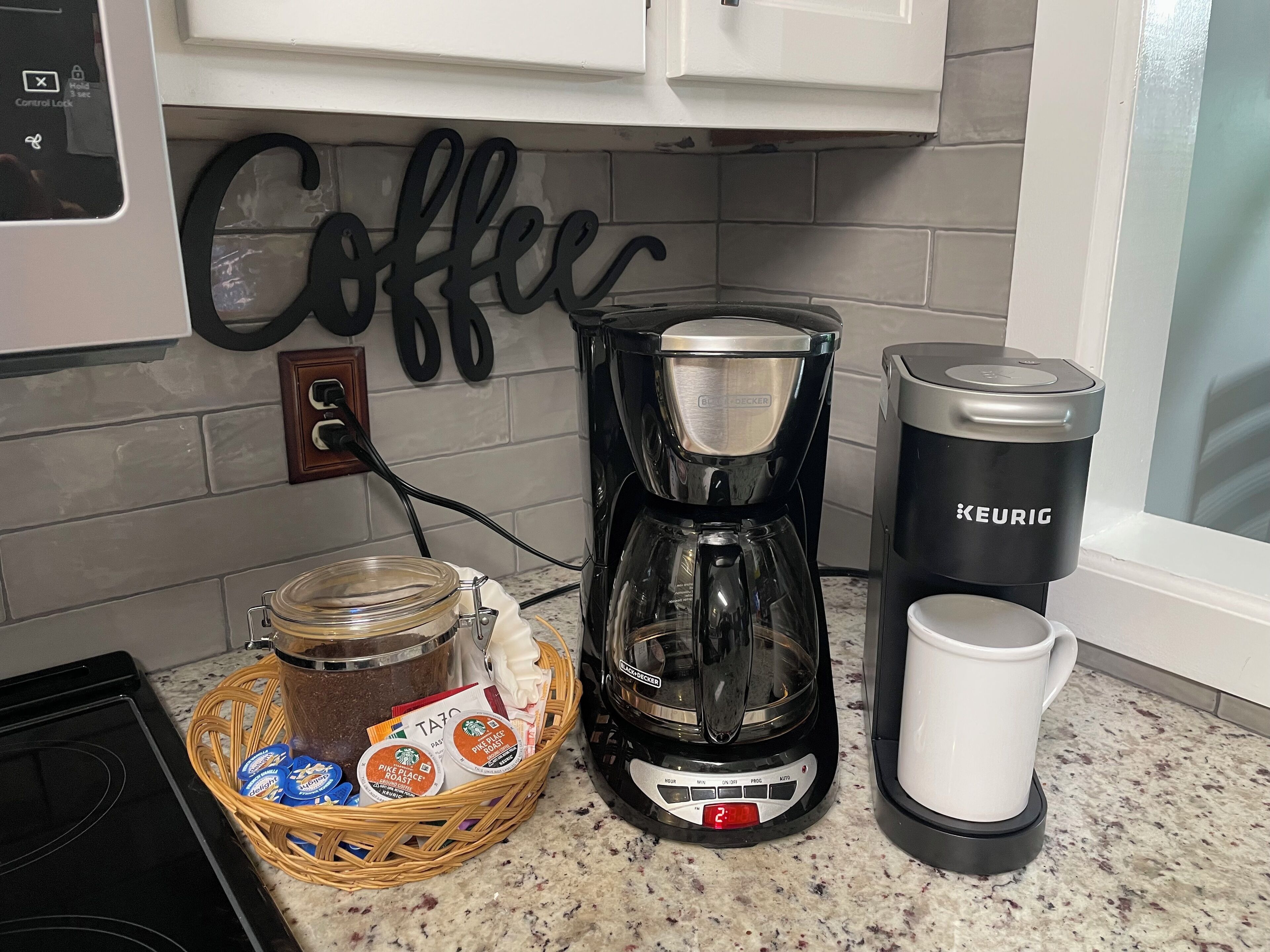 A kitchen with a coffee maker, a Keurig machine, a coffee mug, and a basket of coffee pods.