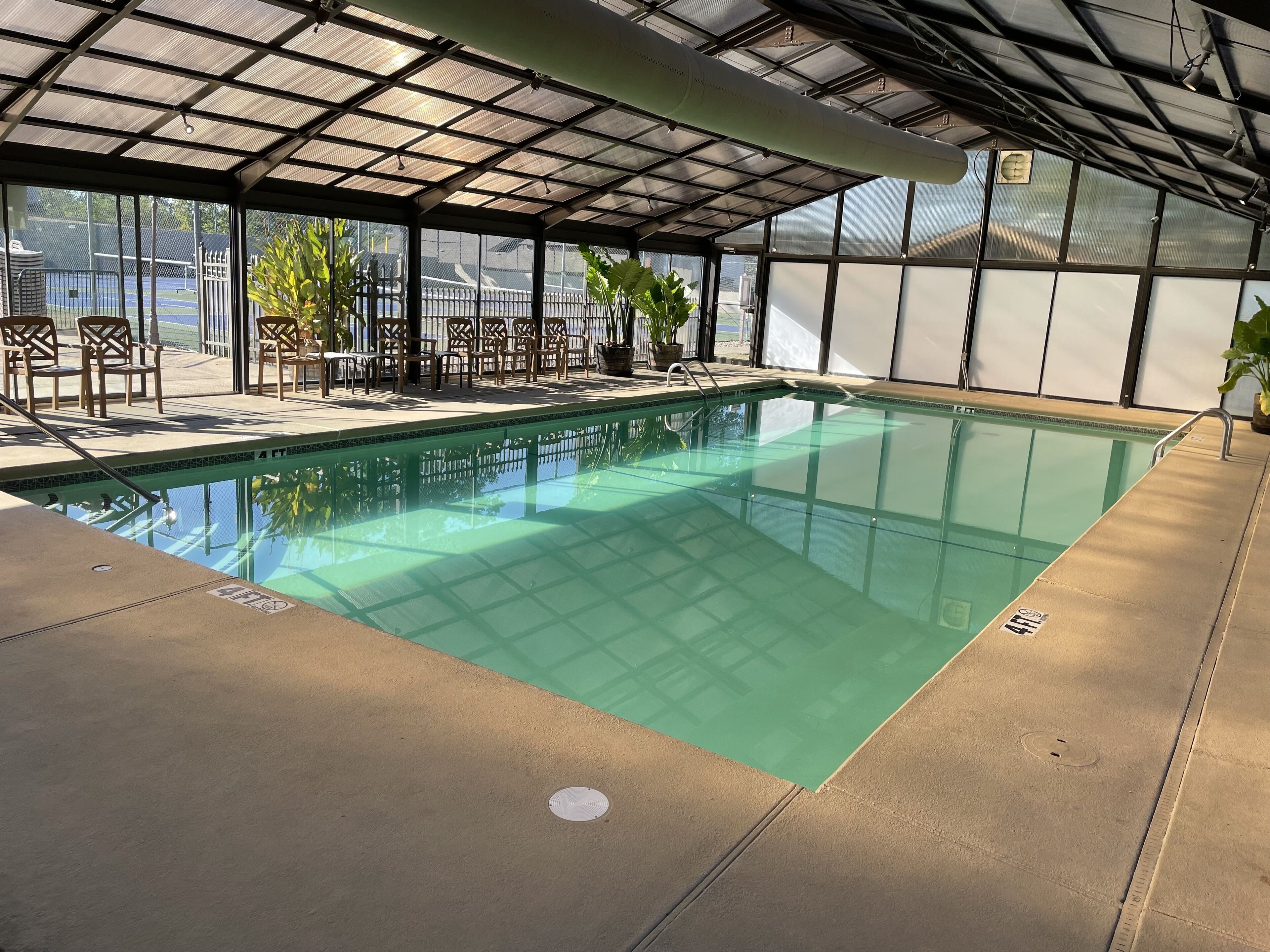 An indoor swimming pool with clear water, surrounded by chairs and potted plants.