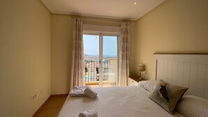 A hotel room with a large bed, a nightstand, a lamp, and a view of the city through a balcony door.