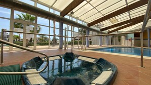 An indoor swimming pool with a hot tub, surrounded by glass walls and a covered roof.