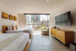 A modern bedroom with two beds, a sofa, a TV, and a view of the city.