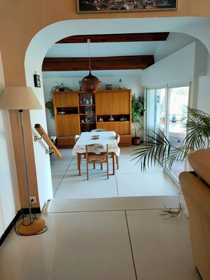 A dining area with a table and chairs, a wooden cabinet with various items, and a view through an archway to an outdoor space.