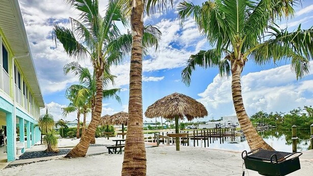 A beachfront area with palm trees, a pool, and a barbecue grill. - Deluxe King Suite w/Deck (Saint James City)