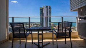 A balcony with a table and chairs, overlooking a cityscape with high-rise buildings and a body of water.