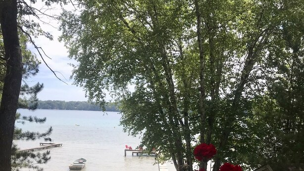 A deck with a table and chairs overlooking a lake, with a boat docked nearby. - Lake front beauty (Hillman)