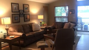 A living room with a brown leather sofa, a coffee table, and a chair. There are framed pictures on the wall and a lamp on the side table. - Lake front beauty (Hillman)