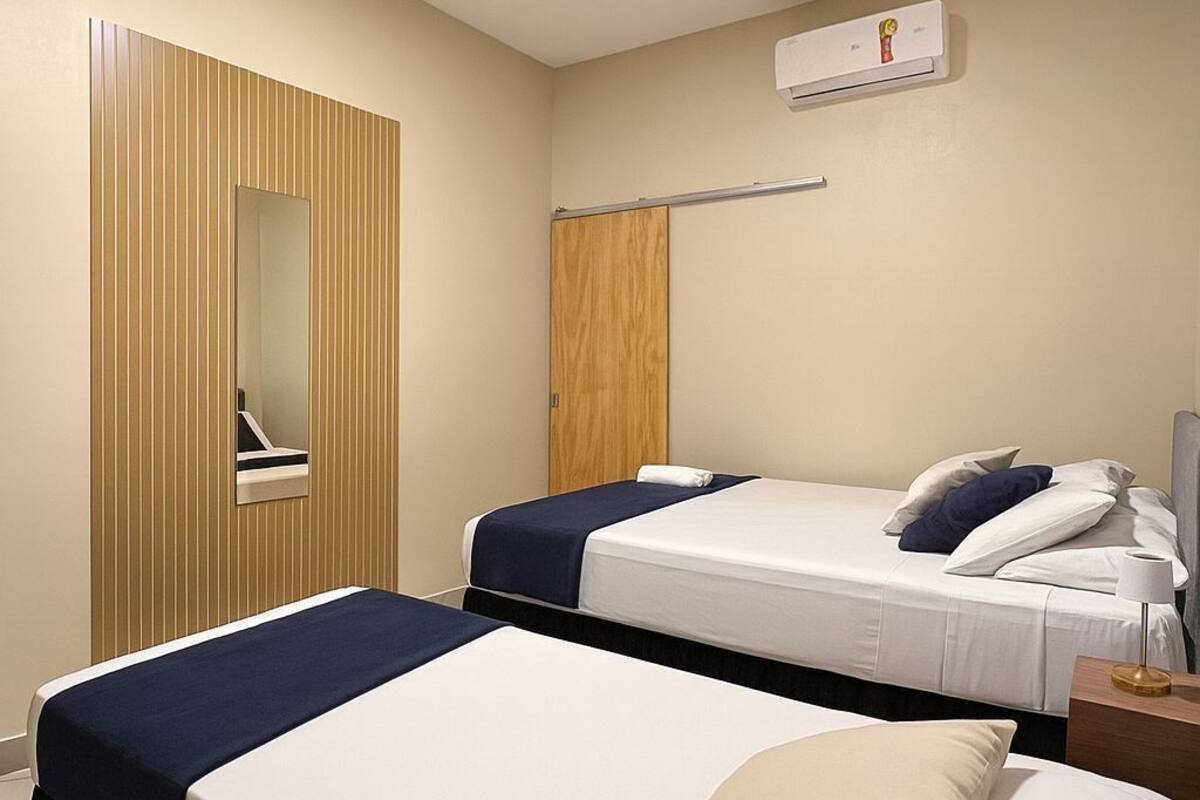 A hotel room with two beds, a mirror, a wardrobe, and an air conditioning unit.
