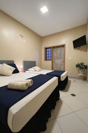 Habitación de hotel con dos camas, un televisor montado en la pared y una planta en maceta.