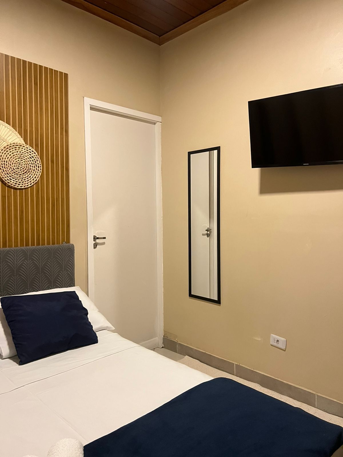 Une chambre à coucher avec un lit, un téléviseur fixé au mur, une porte et un miroir.