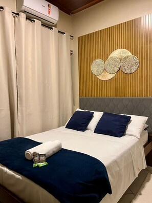 Una habitación de hotel con una cama, aire acondicionado de pared y un panel decorativo en la pared.