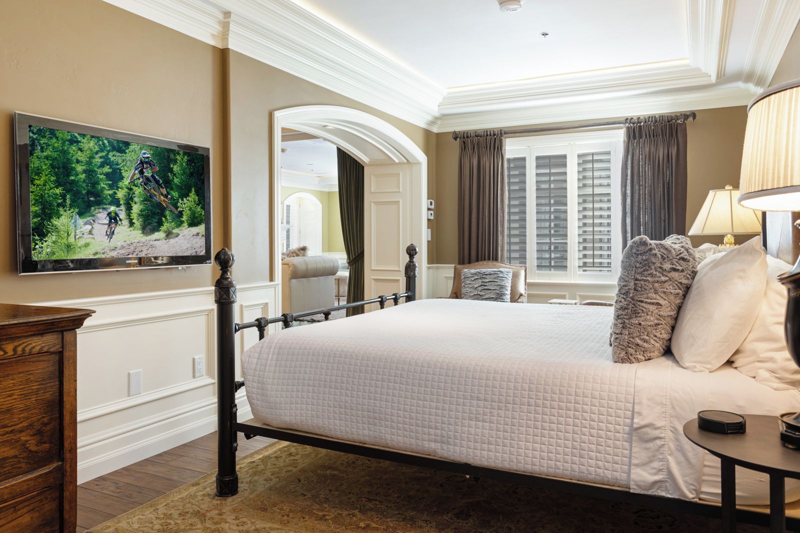 A hotel room with a large bed, a television mounted on the wall, a wooden nightstand, and a window with curtains.
