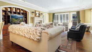 A spacious living room with a beige sofa, a fireplace, a television, and a large window with shutters. - Charlie's Slopeside: Luxury Ski-In/Out, BC Village, Sleeps 8, 3 King Beds, AC, Walk to Everything (Beaver Creek)