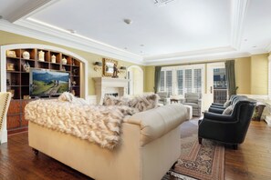 A spacious living room with a beige sofa, a fireplace, a television, and a large window with shutters. - Charlie's Slopeside: Luxury Ski-In/Out, BC Village, Sleeps 8, 3 King Beds, AC, Walk to Everything (Beaver Creek)