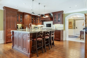 A spacious kitchen with wooden cabinetry, a central island with bar stools, and a large window providing natural light.