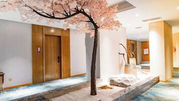 A hotel lobby with a cherry blossom tree, wooden doors, and a stone water feature.