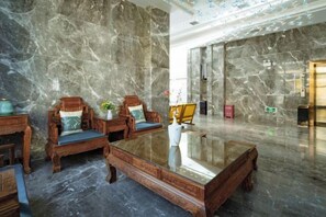 A lobby with marble walls, wooden furniture, and a glass coffee table. - Xingzhike Hotel (Wuchuan)