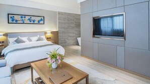 A modern bedroom with a large bed, bedside tables, a flat-screen TV mounted on the wall, and a small table with a vase of flowers. - Xingzhike Hotel (Wuchuan)