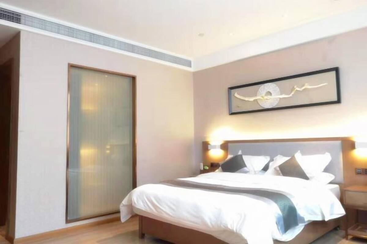 A hotel room with a bed, bedside tables, a wall-mounted artwork, and a sliding door.