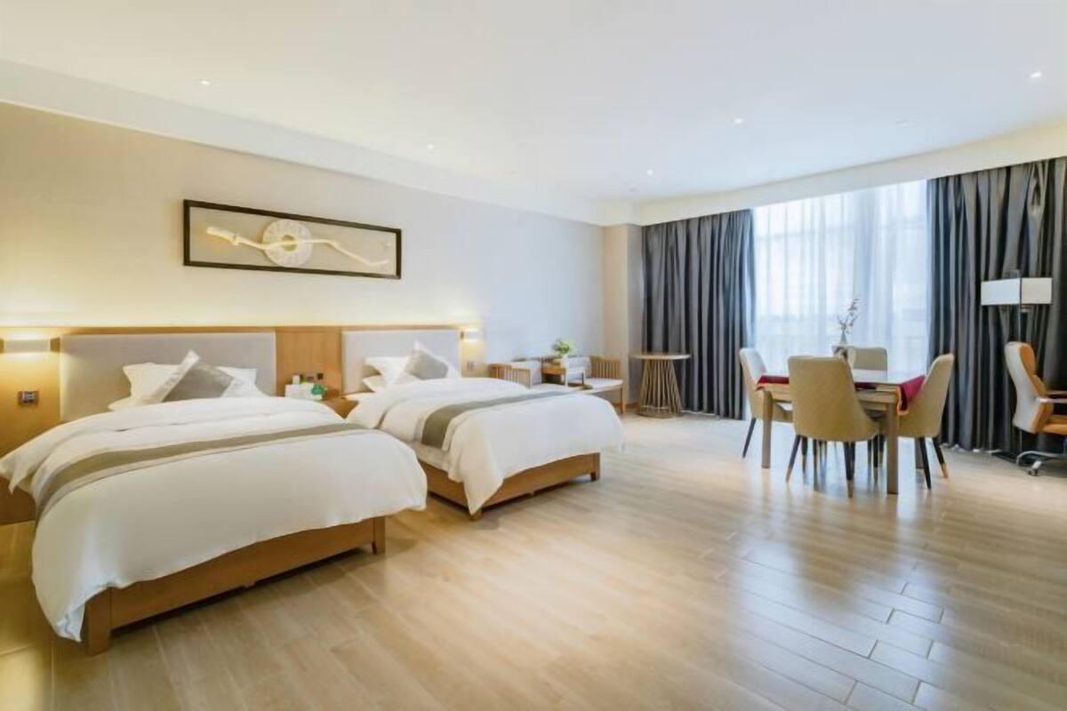 A hotel room with two beds, a dining area with chairs, a table, and a large window with curtains.