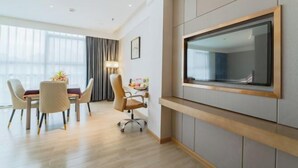 A modern hotel room with a dining area, a flat-screen TV mounted on the wall, and a large window with curtains. - Xingzhike Hotel (Wuchuan)