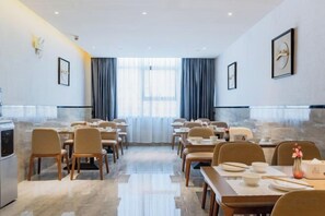 A hotel dining area with tables and chairs, a kitchen, and a view through large windows. - Xingzhike Hotel (Wuchuan)