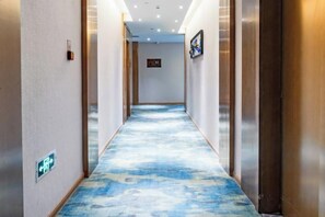 A hotel corridor with a carpeted floor, wooden doors, and a sign on the wall. - Xingzhike Hotel (Wuchuan)