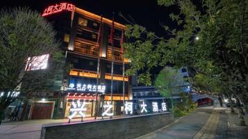 Un hotel de varios pisos con señalización iluminada, fachada de ladrillo y un camino pavimentado.
